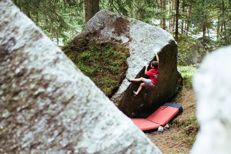 Boulderer an einem moosigen Block im Wald mit Crashpad