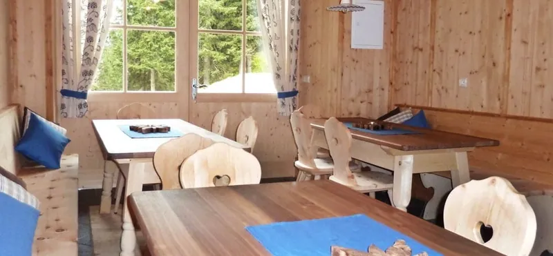 Die Stube der Hofschenke mit Holztischen und blauen Sitzkissen